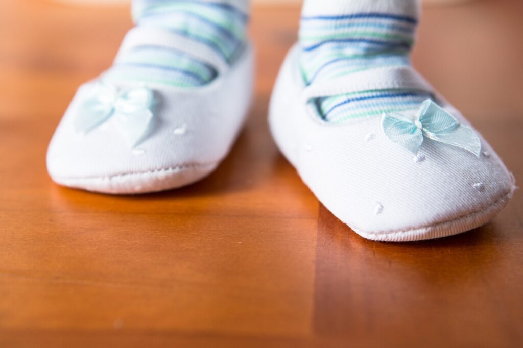 Babyfüße in weichen weißen Stoffschuhen mit Schleife auf Holzboden