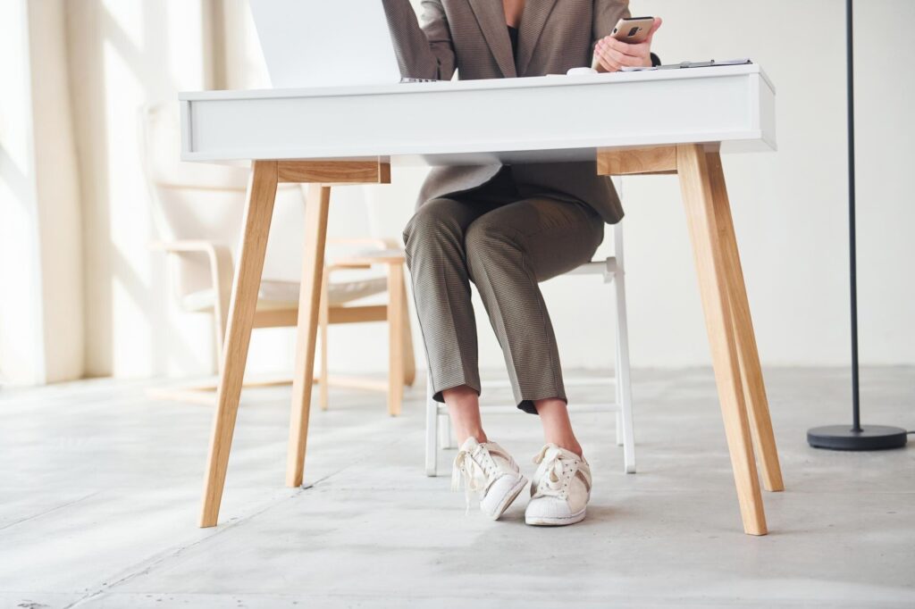 Eine Frau sitzt am Schreibtisch, an den Füßen weiße Sneaker
