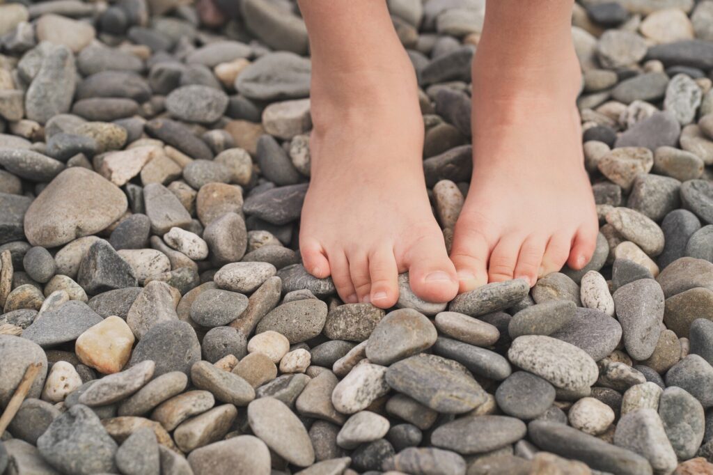 Nackte Kinderfüße stehen auf grauen Kieselsteinen
