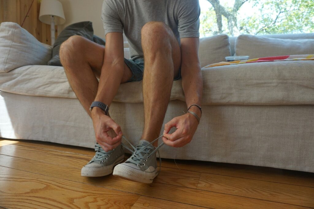 Mann sitzt auf einem hellen Sofa und schnürt graue Stoffsneaker