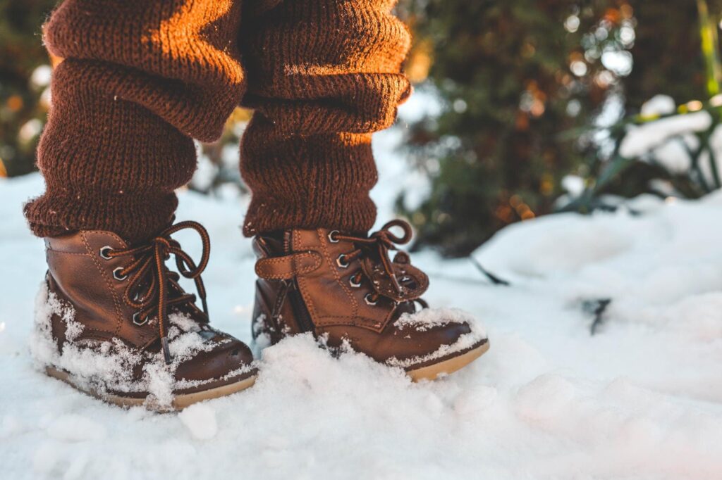 Kinderbeine in Strickhose und braunen Winterstiefeln im Schnee