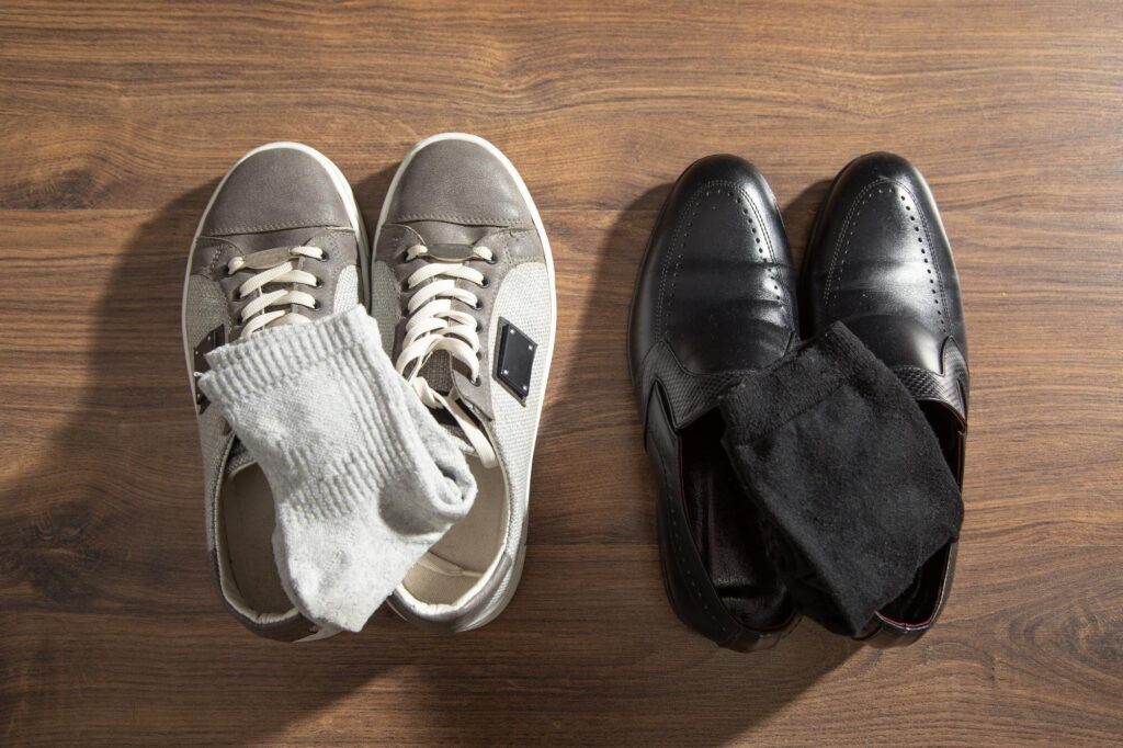 Zwei Paar Schuhe nebeneinander auf Holzboden: graue Sneaker und schwarze Lederschuhe