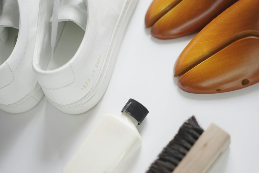 Weiße Ledersneaker, hölzerne Schuhspanner, Reinigungsflasche und Bürste auf weißem Grund