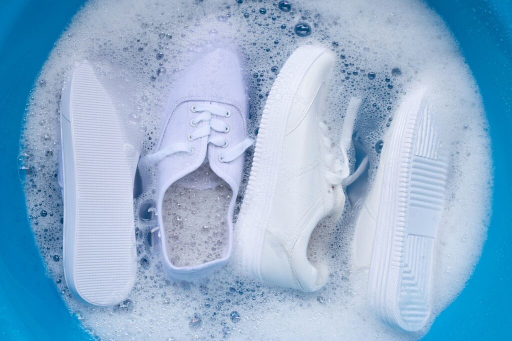 Weiße Stoffschuhe weichen in einer Schüssel mit Seifenwasser ein